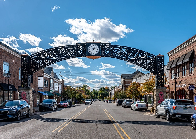 Cars navigate a lively street featuring a prominent clock in the background.